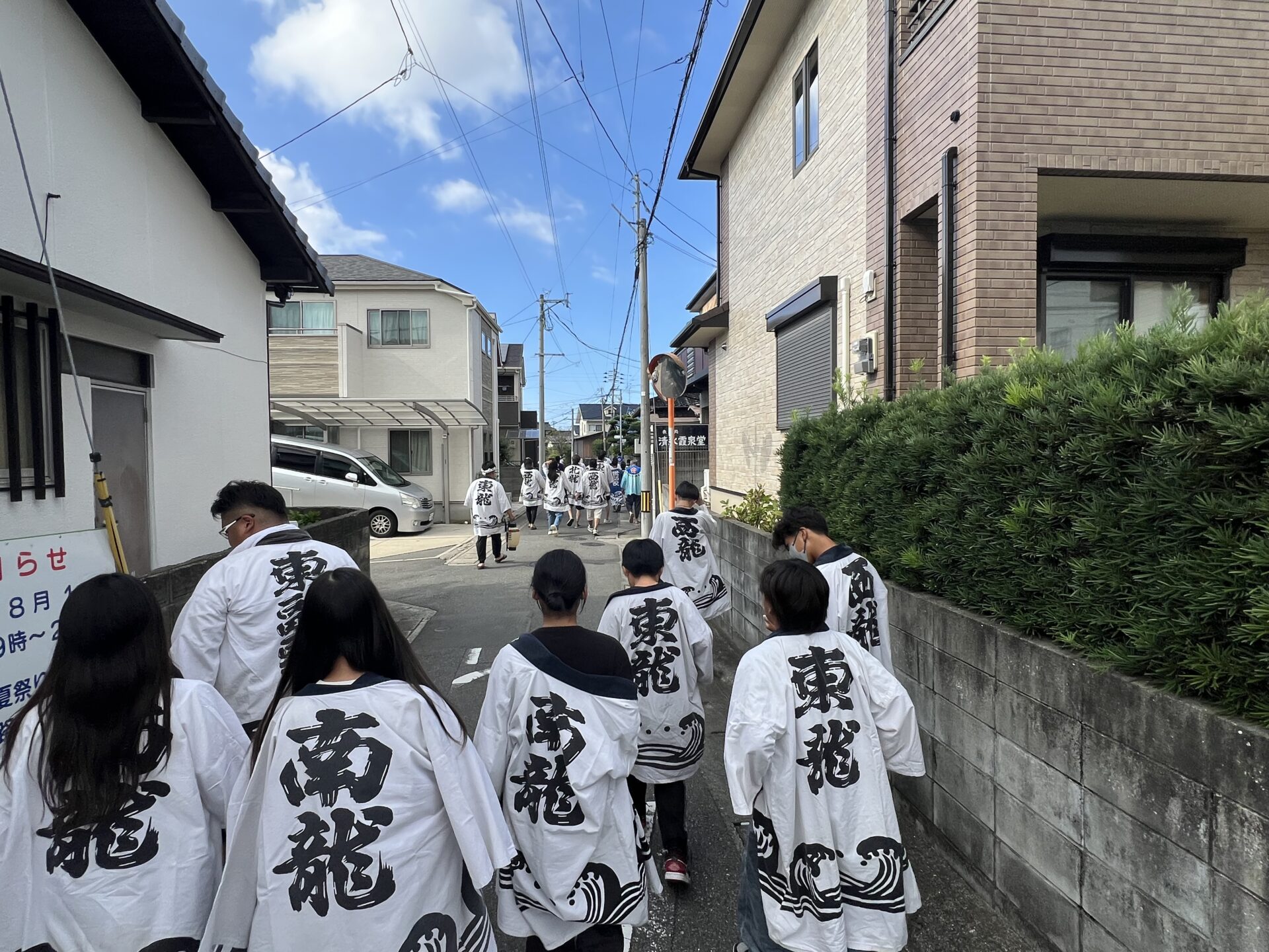 住宅街を進む初盆参りの行列。見守る人、手を振る人